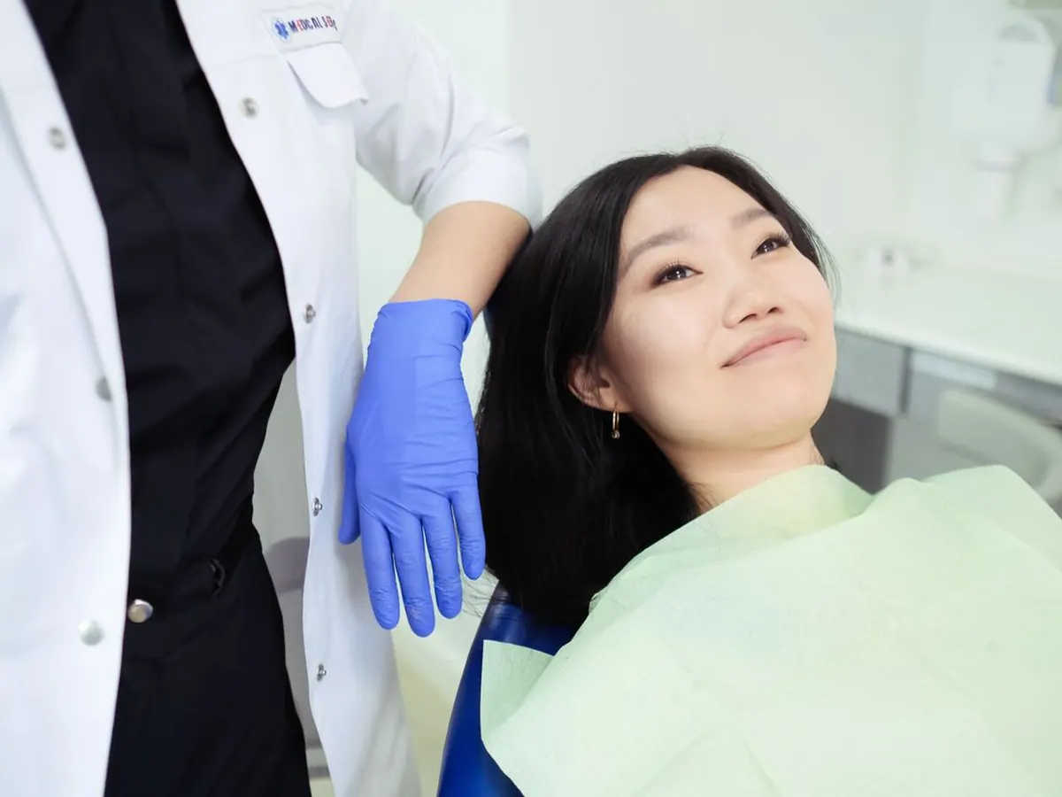Pasien perempuan bersantai di kursi perawatan gigi, dokter menenangkan dengan tangan di bahunya
